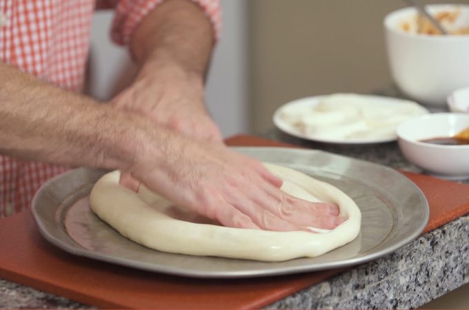hand spreading pizza dough on pizza pan