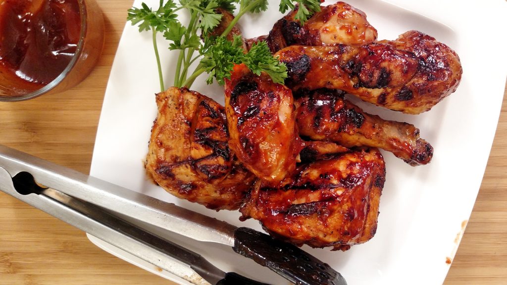 Indoor BBQ Chicken Grill on white plate with tongs, bbq sauce, parsley, bamboo cutting board