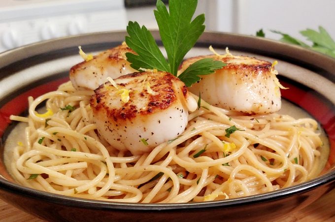 Seared Scallops on pasta plated in bowl with parsley garnish