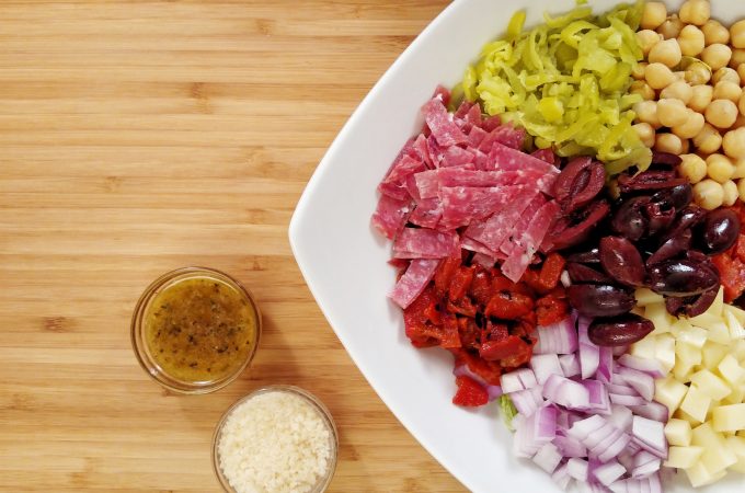 Italian Chopped Salad in a white bowl. pepperocini, salami, pepperoni, onions, cheese, garbanzo beans, roasted red peppers, Italian dressing