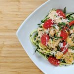 Zoodle Lemon Chicken with zoodles, tomatoes, lemon , chicken on white plate on bamboo cutting board