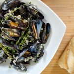 A bowl of blue/black mussels with a crusty baguette. Classic French mussel recipe with Garlic, shallots and thyme flavor the dish.