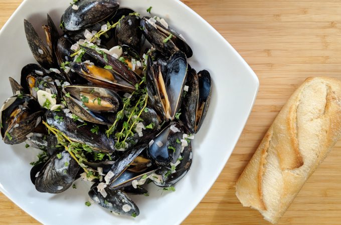 A bowl of blue/black mussels with a crusty baguette. Classic French mussel recipe with Garlic, shallots and thyme flavor the dish.