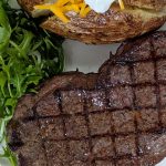 Steak with grill marks on a white place with a salad and baked potato