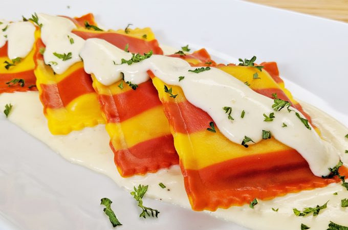 Red and Yellow Striped Lobster Ravioli with Cream Sauce plated on white plate with parsley