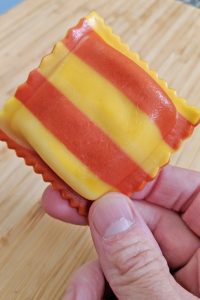 Red and Yellow Striped Lobster Ravioli with Hand and Bamboo Cutting Board