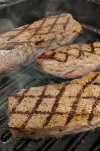 Steak with diamond sear marks on a cast iron grill pan with smoke