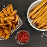 Baked French Fries on a white plate and Fried french fries in a fry basket with ketchup on a black background