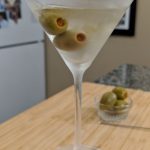 martini in a martini glas with olives on a wood cutting board