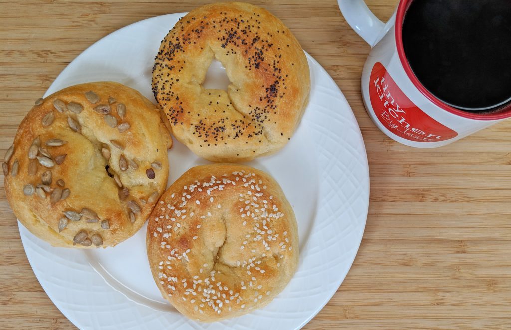 Overhead view of Keto Bagels with Sesame Seeds and Poppy Seeds and Sunflower Seeds on a white plate with a Tiny Kitchen Big Taste Coffee Mug