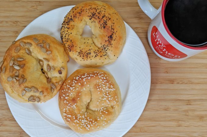 Overhead view of Keto Bagels with Sesame Seeds and Poppy Seeds and Sunflower Seeds on a white plate with a Tiny Kitchen Big Taste Coffee Mug