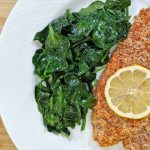 Tiny Kitchen Keto Almond Crusted Fish with lemon and wilted spinach on white plate and bamboo cutting board