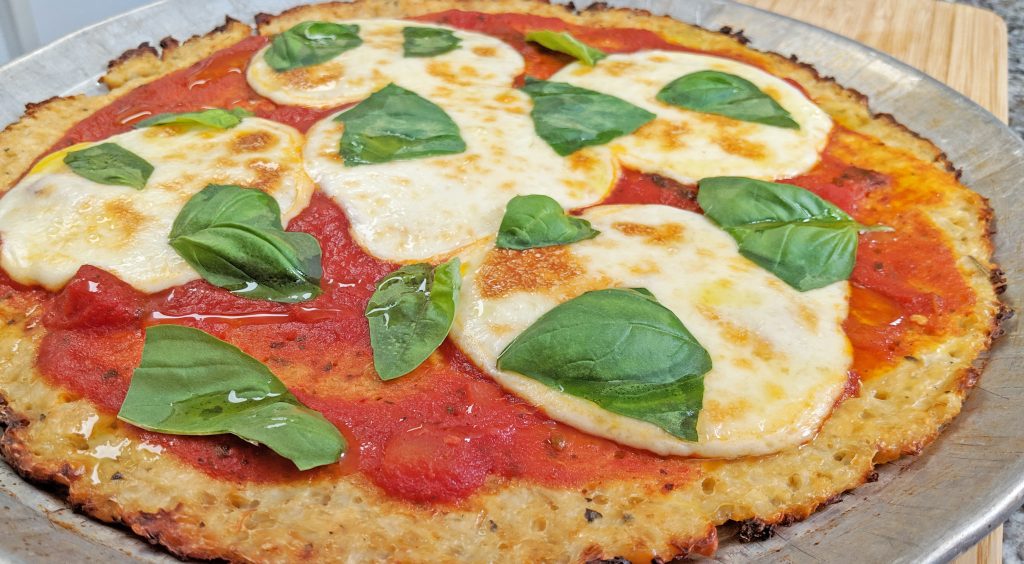 Keto Margherita Pizza with a Gluten Free Cauliflower Crust, mozzarella cheese, fresh basil, tomato sauce on silver pizza pan